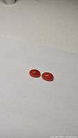 Two small oval cabochon carnelian gemstones on white background, showing the full lot contents.