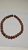 Photo of a round amber bead bracelet on a white background showing polished beads with natural inclusions and varied amber tones.
