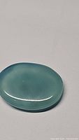 Natural oval cabochon blue chalcedony gemstone shown under natural light on a flat surface, clearly displaying its polished oval shape and glossy icy blue color.