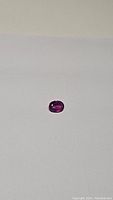 Oval cut bubblegum pink to purple sapphire gemstone on a white surface, showing color and shape.