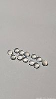 Ten small round white moonstone cabochons arranged in two rows on a white background, showing their size and surface quality.