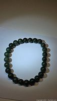 Photo of green jade bead bracelet laid out flat, showing round beads and elastic string