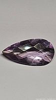 Close-up photo of a pear-shaped, checkerboard cut natural amethyst showing pink-purple colors and faceted surfaces.