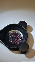 Black dish holding approximately 48 round cabochon cut garnet stones with deep pink-purple color, approx 2mm size.