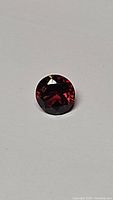 Photo showing round cut cherry red garnet gemstone with deep red color and visible facets.