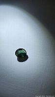 Natural green oval sapphire gemstone under flashlight, showing color and cut details.
