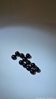 12 round cabochon jet black onyx gemstones arranged on white background, showing smooth surface and uniform size.