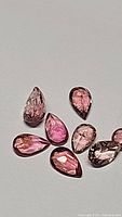 Close-up image of 8 pear cut natural pink tourmaline gemstones with varying shades of pink on white background.