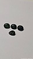 Four natural green-blue sapphires on white background, showing oval and pear shapes.