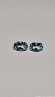 Pair of natural sky blue oval cut topaz gemstones on a plain background, showing color and cut details.