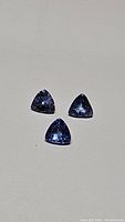 Three natural tanzanite trillion cut gemstones laid on flat surface, showing their shape, color and clarity.