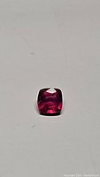 Top-down photo of cushion cut ruby showing its vivid red pink color and square shape with rounded corners.