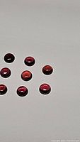 Nine small round cabochon rhodolite garnet gemstones arranged on a white background, showing deep purple-red hues and polished surfaces.