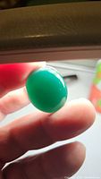 Oval vivid green onyx cabochon gemstone held between fingers showing polished surface and translucent vibrant green color.