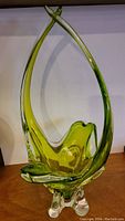 Front diagonal view of the green and clear art glass vase showing teardrop shape and feet base.
