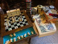 Wide view of the chess set showing carved wooden chess board with Asian motif tiles, resin chess pieces in storage drawer, chess timer, decorative tins and small bowls, plus a painted scroll.