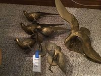 Grouped display of all brass bird figurines on carpet, showing pheasants, stork, and seagull.