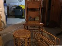 Full view of wooden chair showing carved back and cane seat, bamboo and cane round stool, wicker magazine rack on carpeted floor.