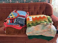 Photo of crochet throw blankets folded and stacked on couch showing varied colors and crochet patterns including zigzag, patchwork, netted, and floral designs.