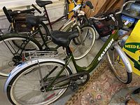 Full side view of green and silver Raleigh cruiser bike with black saddle and basket on front