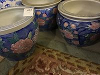 Three heavy ceramic garden pots with blue background and pink floral design, positioned close to each other on the floor.