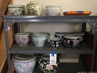 Metal shelving unit with three shelves holding an assortment of garden pots in multiple sizes and floral designs.