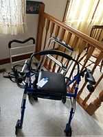 Front and top view of blue Medline Guardian walker on wheels showing black padded seat, hand grips, and part of white bed rails in the background.