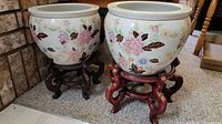Two white round ceramic pots decorated with koi fish and floral patterns on reddish-brown wooden stands