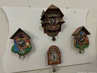 Four mini plastic painted clocks on white background showing front view, varying chalet designs and floral clock