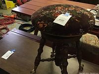 Side angle of the piano stool showing the velvet floral seat upholstery and wooden burl walnut turned legs.