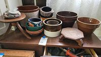 Photo showing the ten assorted pots and crocks along with two wooden stands on a wooden surface.