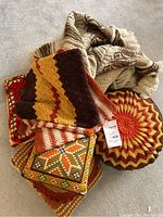 Lot of assorted knit and crochet throw pillows in retro browns, oranges, cream, and beige colors, shown piled together.