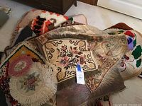 Pile of various rugs in different colors, floral and geometric patterns with fringed edges and thick textures.