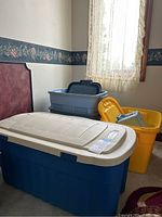 Group photo showing all six plastic storage bins in assorted sizes and colors stacked in a room corner with window and lace curtains.