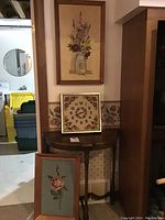 Half moon wooden table with three framed needlepoint artworks arranged behind and on top of it.