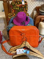 Orange Samsonite bag in front with floral suitcases stacked behind and wooden hangers leaning against the luggage.