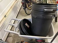 The grey Rubbermaid wheelbarrow loaded with two black DPI 77L garbage bins with lids.