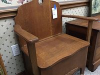 Front angle view of the wooden antique commode chair showing armrests and seat.