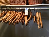 Wide view of collection of wooden hangers on metal rod, multiple wood tones and styles visible including some vintage hangers.