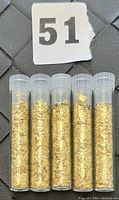 Five small clear glass vials filled with gold flakes, arranged in a row seen from the front.