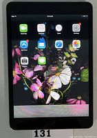 Front view of Apple iPad Mini powered on, showing home screen with apps on display.