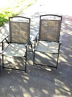 Two lawn chairs placed side by side on pavement in daylight, showing full chairs clearly