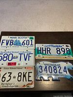 Top view of five Canadian license plates from different provinces and territories laid out on a dark surface.