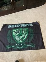 Full view of a black cloth banner with a green and white crest and 'Dropkick Murphys' text above and 'Going Out In Style' below.