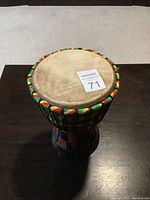 Full view of the Ghanaian djembe drum showing the wooden checkered base and colorful Kente cloth skin with braided rope edges.