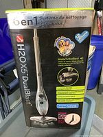 Photo of the unopened box of H2O X5 DualBlast showing the 6-in-1 steam mop and handheld cleaner system and key features in multiple languages.