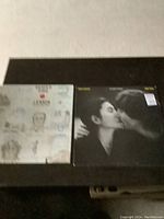 Two John Lennon vinyl record albums, Double Fantasy on the right and Shaved Fish on the left, displayed side by side on a dark surface.