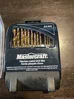 Closed black plastic case with Mastercraft branding and 21 titanium-coated drill bits visible through transparent window.