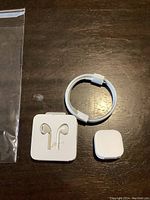 Full view of Apple EarPods, Lightning charging cable, and silicone ear tip replacement case on a dark wooden surface.