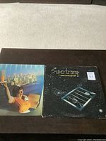 Photo of both Supertramp LP albums laid out side by side on a dark wood surface.